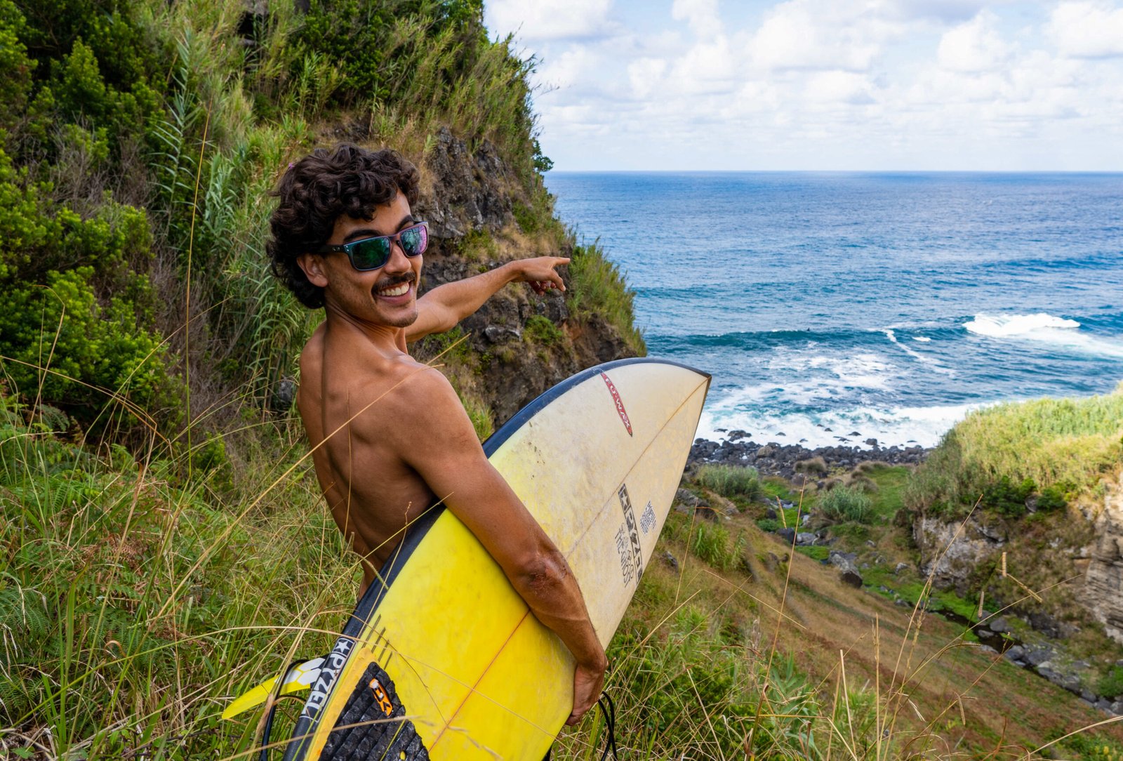 Local surfer hiking with a surfboard and pointing toward incoming waves