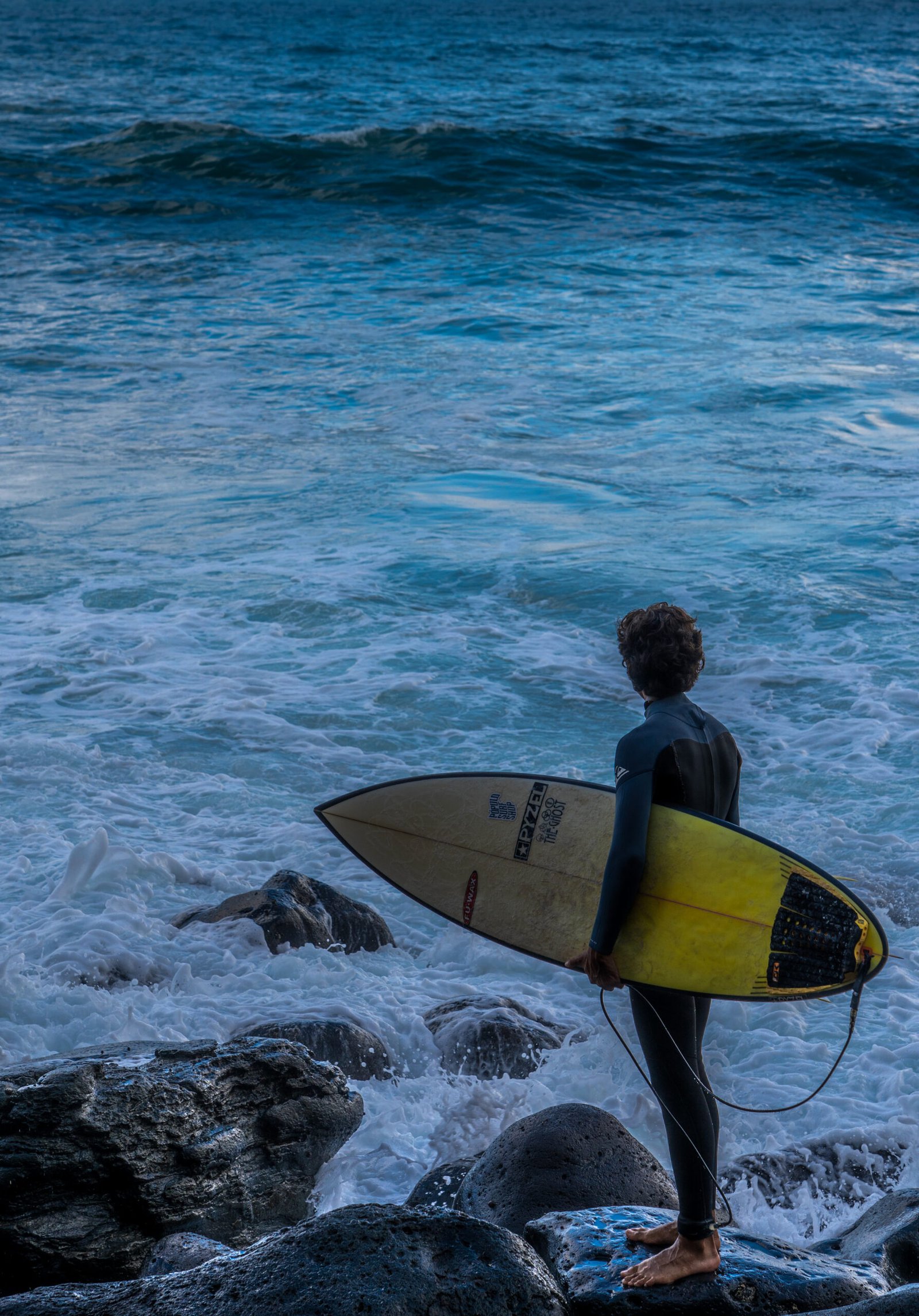 Local surfer standing on the rocks waiting for the right moment to enter the water