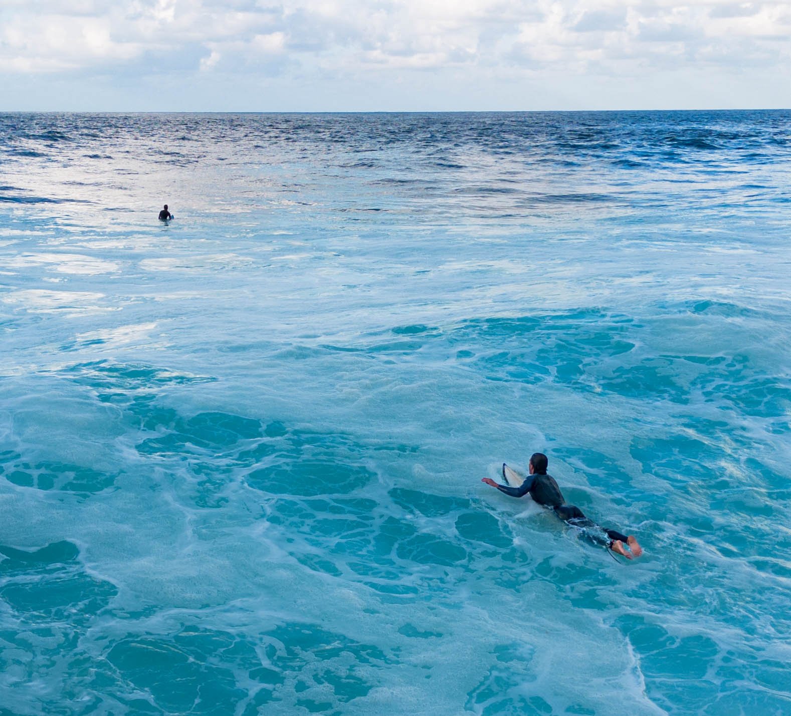 Two surfers paddling and waiting together as clean swell lines approach