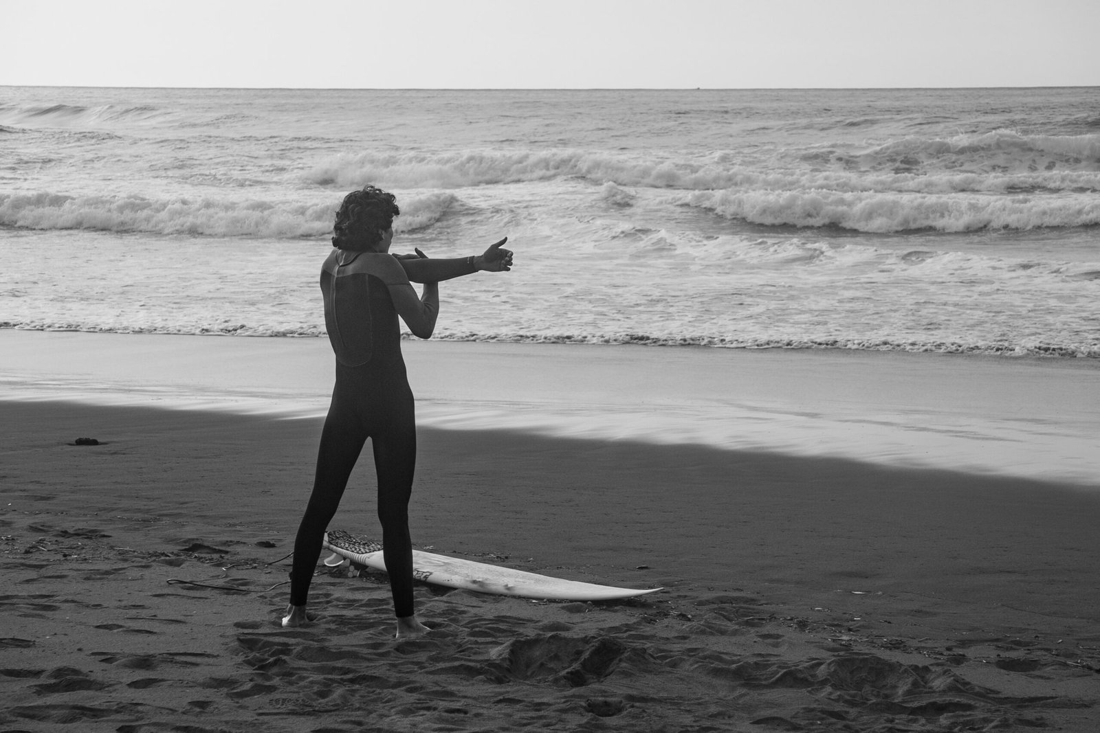 Surfer stretching on the beach while watching the ocean before a session