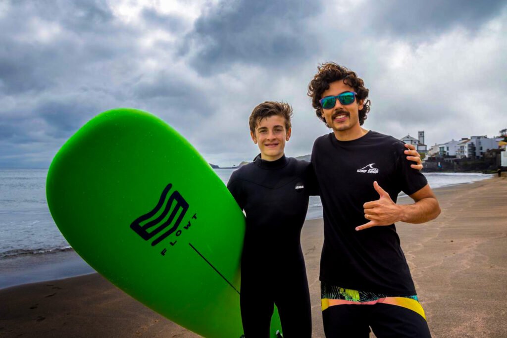 Surf instructor Caio Mendes celebrating a beginner surf lesson with a child surfer holding a soft-top board