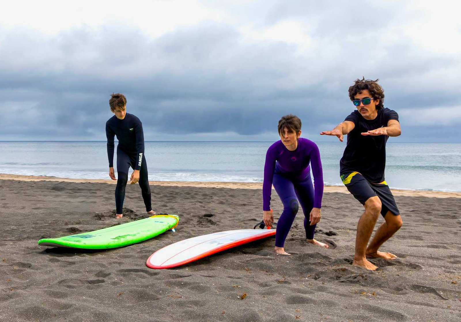 Surf instructor Caio Mendes teaching proper surf stance to beginner surfers on the beach in the Azores