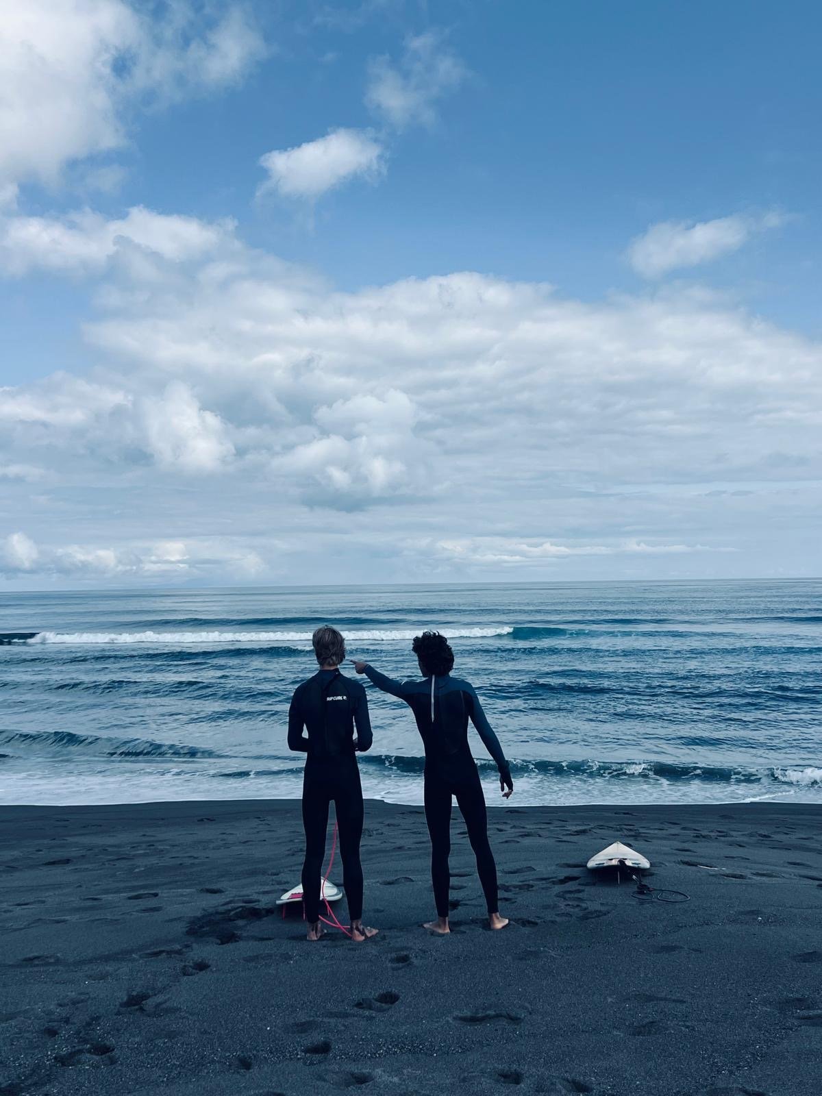 Local surf guide pointing out wave lines to an intermediate surfer on the beach