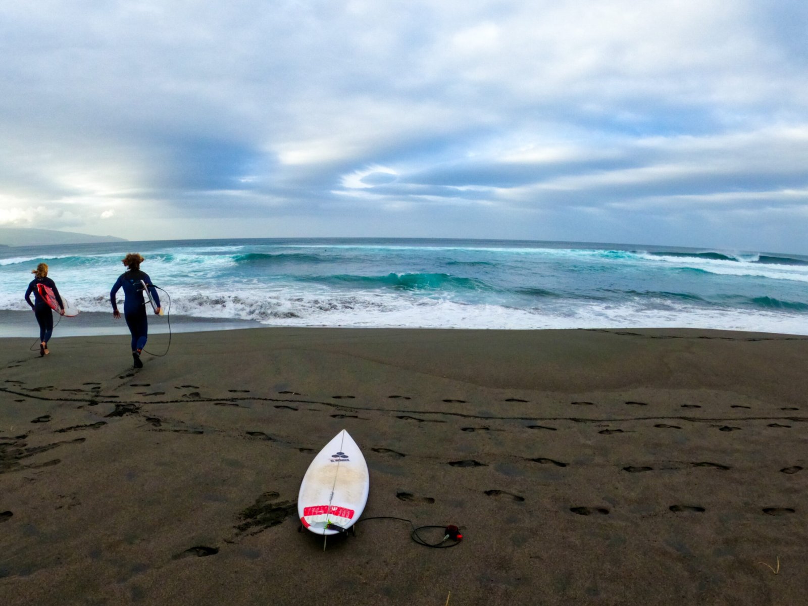 Two surfers running to the water with their surfboards
