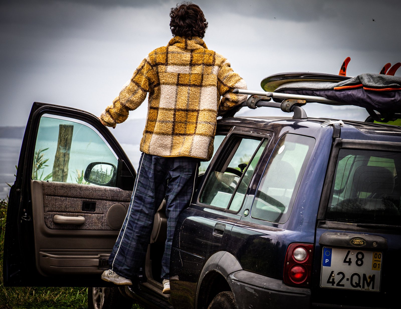 A surfer watching the ocean on top of his Land Rover pick up truck