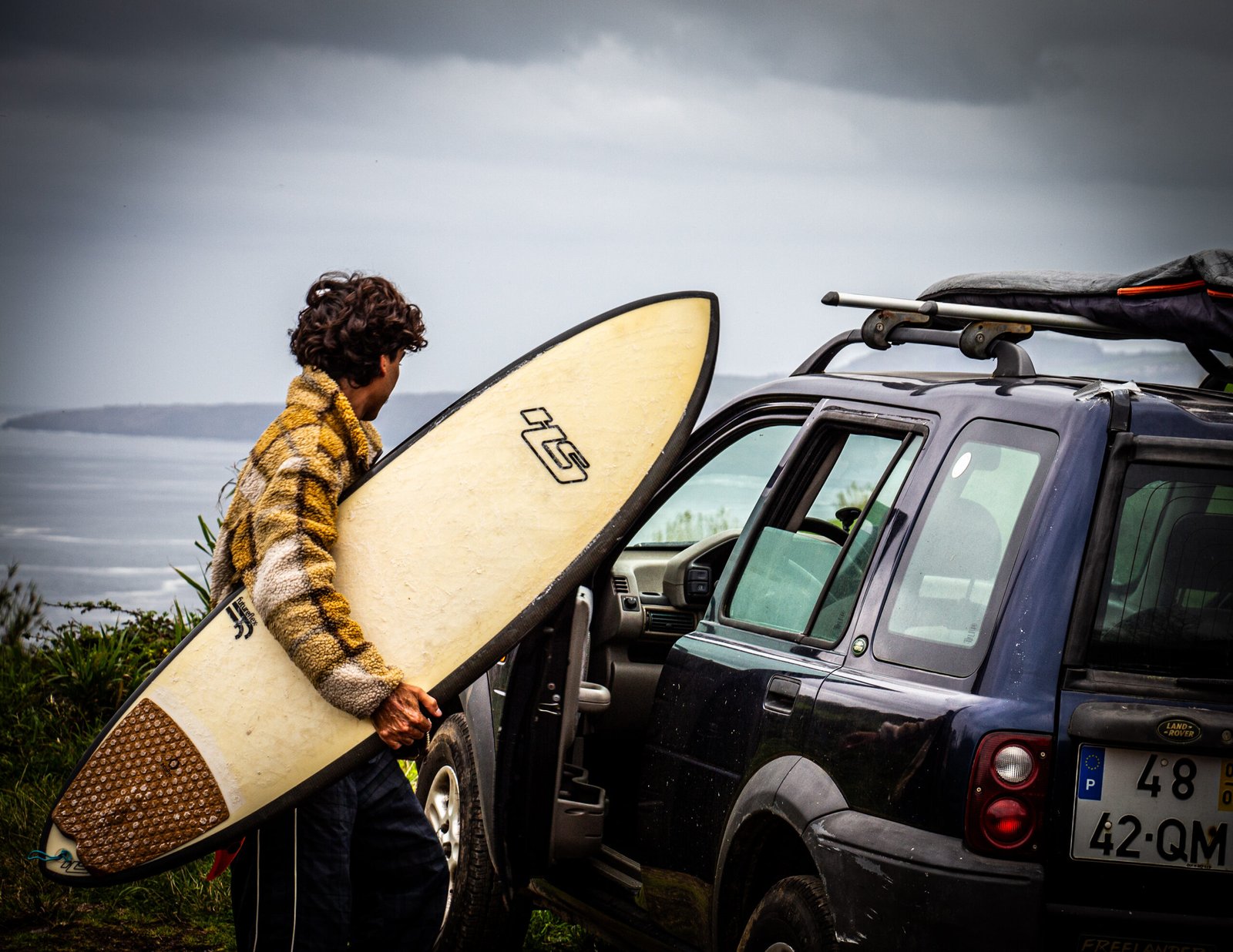 a surfer carrying taking his surfboard out of the car